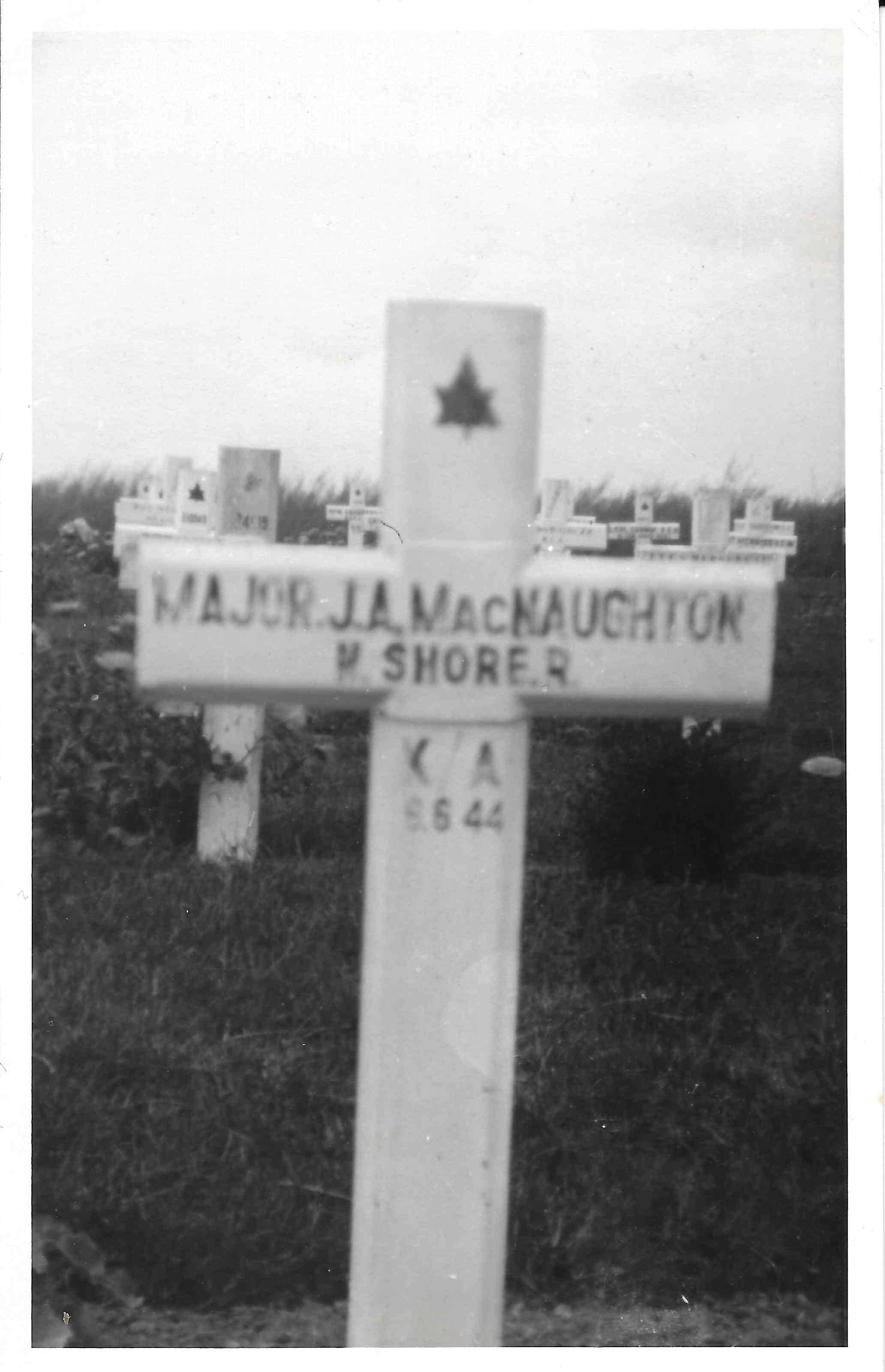 A black and white image shows a white cross grave marker.
